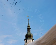 Campanile su cielo azzurro con stormo di uccelli in volo